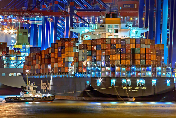 Ein beleuchtetes, volles Containerschiff au der Elbe in der Nacht