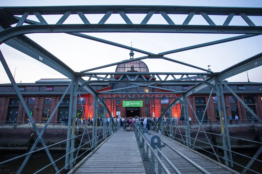 Fischauktionshalle von der Wasserseite im Vordergrund der Fähranleger mit Besuchern bei einer Firmenfeier im Sommer organisiert von der Eventagentur Hamburg