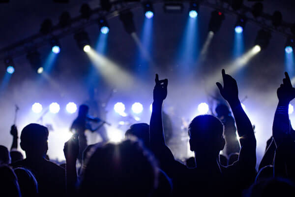 Feierndes Publikum von hinten im Gegenlicht vor einer blau beleuchteten Bühne mit musizierenden Musikern