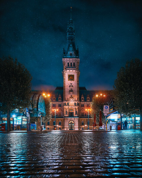 Nächtliches festlich beleuchtetes Hamburger Rathaus im Vordergrund regennasses Kopfsteinpflaster