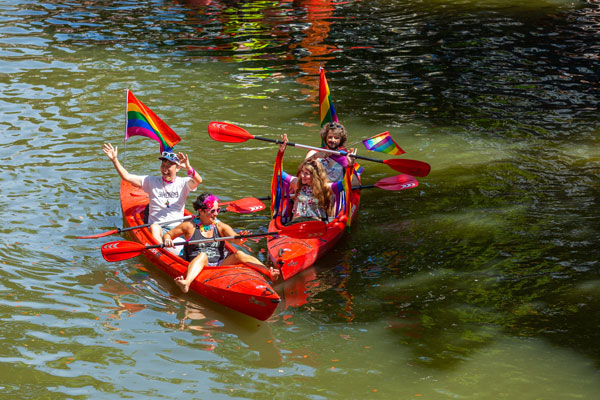 Zwei Knallrote Kanus mit vier fröhlichen Personen auf einem gründlichen Fluss im Sommer. Kanufahren Kajakfahren auf der Alster und den Fleeten in Hamburg und Umgebung als Betriebsausflug und Firmenfeier