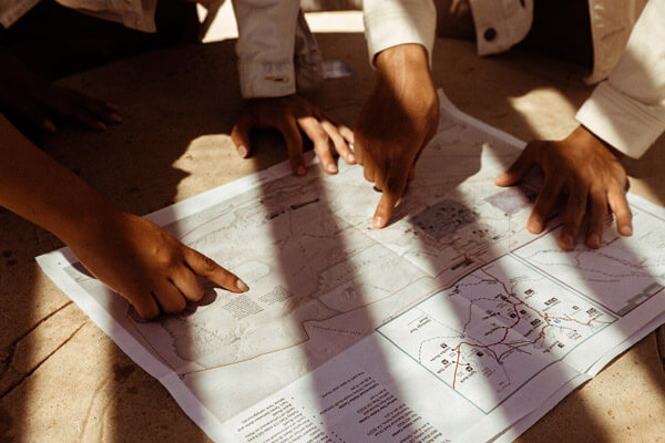 Zwei Menschen und vier Hände zeigen auf eine Landkarte die in Sonnenlicht auf einem Holztisch liegt. Unterhaltung und Spiel bei einem Betriebsausflug im Norden, durchgeführt von der Eventagentur Hamburg